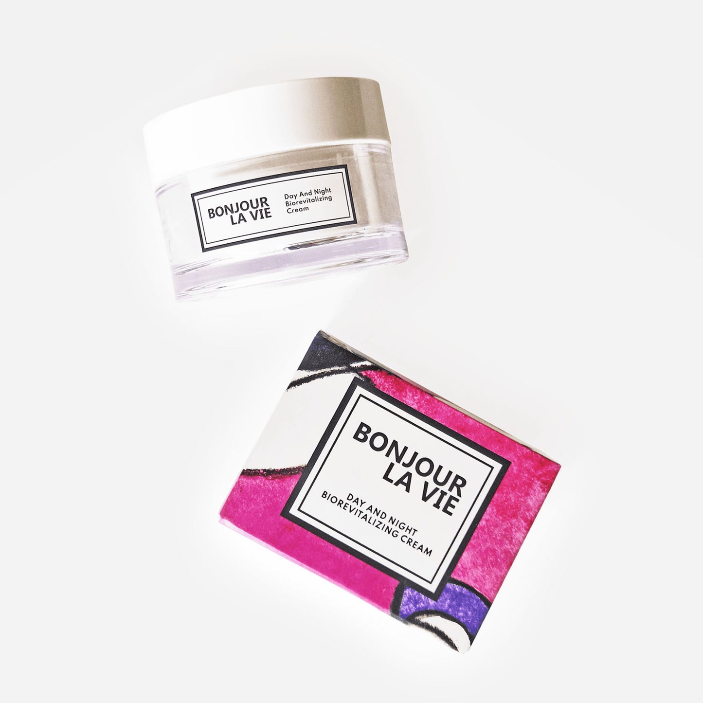 Immagine del vaso da 50 ml con tapppo bianco e vaso trasparente e della scatola colorata con toni porpora e fucsia della Crema BioRevitalizzante Giorno e Notte di Bonjour La Vie su fondo bianco