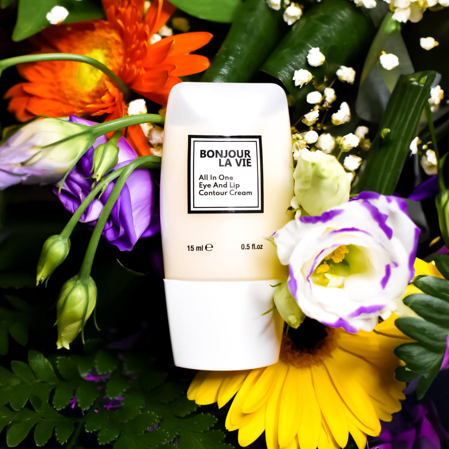Immagine del Flacone di 'Bonjour La Vie - All In One Eye And Lip Contour Cream' da 15 ml tra fiori viola, gialli, arancioni e piccoli fiori bianchi 