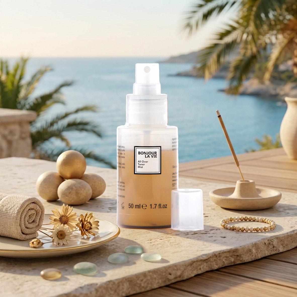All Over Toner Mist 50 ml Bonjour La Vie su ripiano in pietra con incenso, fiori secchi e vista mare con palme sullo sfondo.