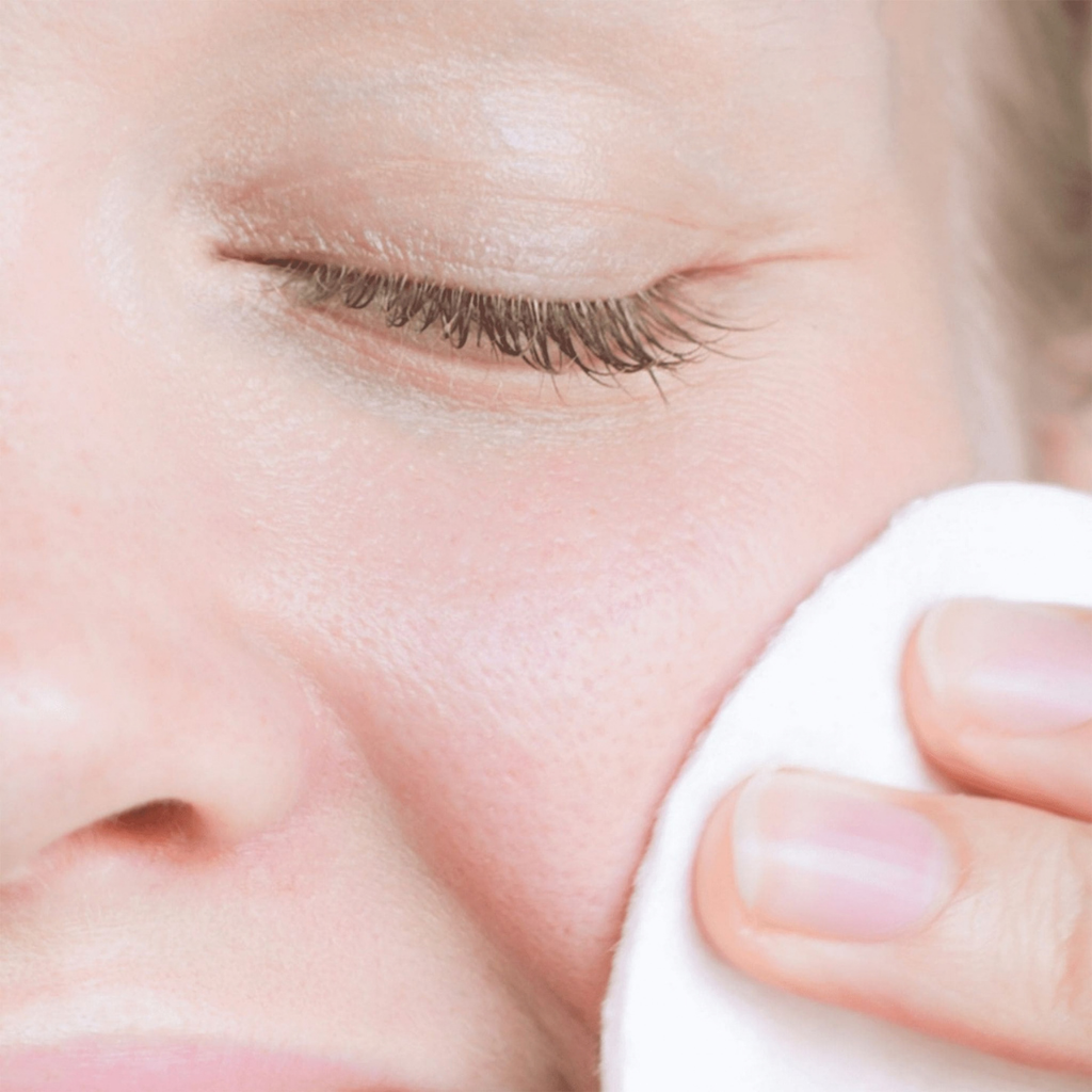 Applicazione di Biphasic Make Up Remover Bonjour La Vie con dischetto di cotone sul viso vicino all’occhio chiuso.